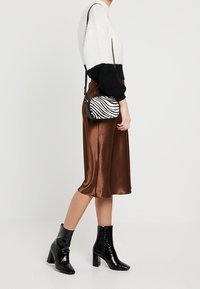 Krémový a černý pletený svetr, hnědá saténová midi sukně, černé lakované kotníkové boty a kabelka přes rameno se zebrovým vzorem.