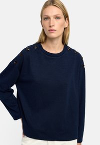 Granatowy sweter wykonany z miękkiego materiału, z okrągłym dekoltem i dekoracyjnymi guzikami wzdłuż szwów ramion.