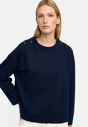 Granatowy sweter wykonany z miękkiego materiału, z okrągłym dekoltem i dekoracyjnymi guzikami wzdłuż szwów ramion.