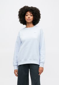 Világoskék pulóver, kerek nyakkal és bordás mandzsettával, sötétszürke nadrággal párosítva. Puha tapintás, minimális logó a mellen.