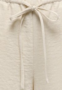 Gros plan sur un pantalon en tissu beige avec une taille élastique et un cordon noué au centre devant.