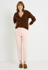 Cardigan marrón con escote en V, tres botones y puños acanalados, combinado con pantalones de pana rosa claro, remangados en los tobillos. Mocasines marrones.