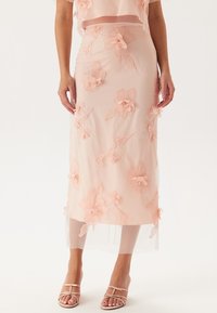 Persikofärgad blyertskjol i genomskinligt material, med strukturerad blommig brodyr och en något genomskinlig design.