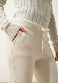 Krämfärgade stickade loungbyxor med dragsko i midjan, med sidofickor och ribbat mönster. Tyget verkar mjukt och mysigt.