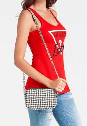 Czarna i biała torba crossbody w wzór houndstooth o eleganckim kształcie i łańcuszkowym pasku, noszona przez osobę w czerwonym topie na ramiączkach i niebieskich dżinsach.
