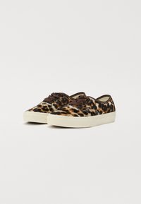 Sneakers z płótnem w panterkę z brązowymi sznurowadłami, okrągłymi noskami i białymi gumowymi podeszwami, z przeszywaną krawędzią w pobliżu górnej części.