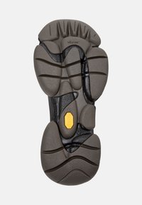 Suola Vibram con un motivo grigio testurizzato, scanalature di battistrada distinte e un accento di logo giallo. Resistente, progettata per aderenza e comfort.