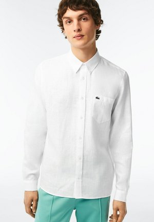 Weißes Langarmhemd aus Leinen mit Button-Down-Kragen, einer Brusttasche auf der linken Seite und einem kleinen Logoakzent. Musterfreies Design.