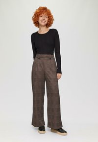 Zwarte geribbelde langermige top gecombineerd met losse, geruite high-waisted broek in grijs, bruin en rood, met twee knopen aan de voorkant. Zwarte sneakers.
