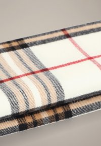 Kraciasta szal wykonana z miękkiego materiału; ozdobiona beżowo-czarnymi i czerwonymi kratkami na kremowym tle. Krawędzie są starannie wykończone.