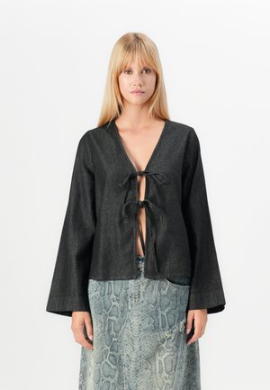 Black denim blouse with long sleeves, deep V-neck, and front tie closure. Worn over a textured blue-green snake print skirt.