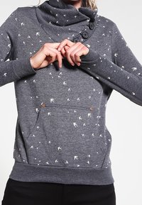 Sweat-shirt gris à col châle en tissu doux, avec des motifs d'oiseaux blancs, des boutons décoratifs et une poche avant à pressions décoratives.