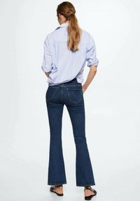 Jeans de mezclilla acampanados en azul oscuro con una textura suave. Combinados con una camisa de rayas azul claro, que presenta mangas enrolladas y un corte relajado.