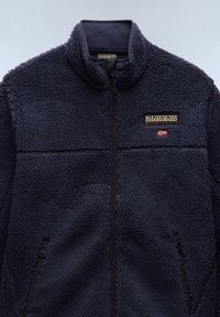 Chaqueta de forro polar azul marino con cremallera completa en la parte delantera, dos bolsillos con cremallera y logotipo Napapijri Geographic con una pequeña bandera en el pecho.