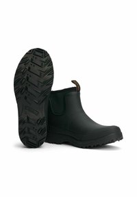 Musta kuminen nilkkurit, joissa on teksturoitu ulkopinta ja siksak-muotoilu pohjassa. Varustettu vetokielekkeellä helppoa pukemista varten.