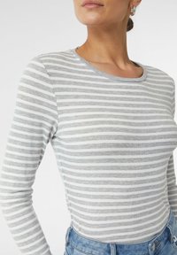 Grau- und weiß gestreiftes Langarmshirt mit Rundhalsausschnitt, aus weichem Stoff, kombiniert mit Jeans.