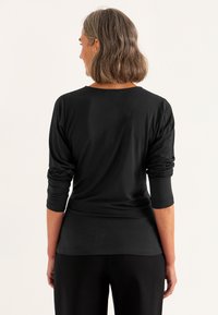 Schwarzes Langarmshirt aus glattem Stoff, mit einer lockeren Passform, hochgeschlagenen Ärmeln und einem runden Halsausschnitt.