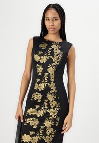 Rochie neagră cu broderie florală aurie pe față, design fără mâneci și siluetă ajustată. Material neted cu o ușoară strălucire.