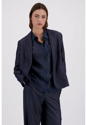 Marineblå jakkesætjakke med en let tekstureret stof, skræddersyet pasform og to lommer. Båret over en matchende marineblå skjorte.