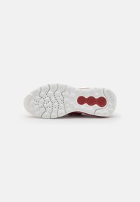 Suola di una scarpa sportiva rossa con una superficie in gomma bianca testurizzata. Presenta motivi circolari per la presa e canali per la flessibilità.