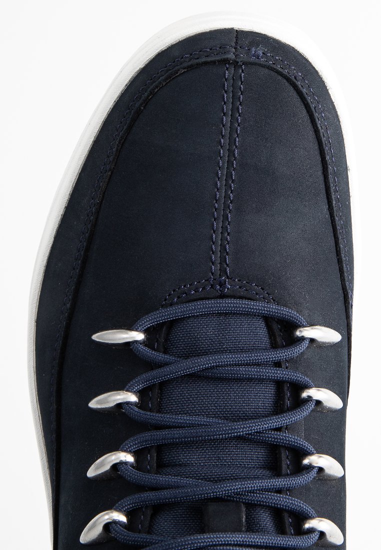 Sneaker in suede blu navy con occhielli argentati, lacci piatti blu navy e suola in gomma bianca con dettagli di cucitura visibili.