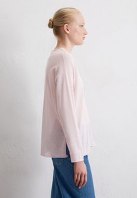 Helles rosa Langarmshirt aus weichem, leichtem Stoff mit lockerer Passform, abgerundetem Saum und subtiler Farbverlauf zu einem helleren Farbton am unteren Rand.