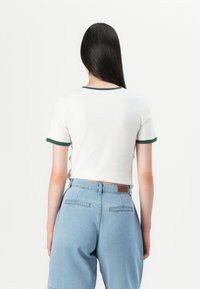 White short-sleeve t-shirt with green trim, paired with light blue denim high-waisted shorts featuring two back pockets.