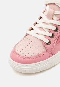 Baskets en cuir rose avec des détails perforés, lacets blancs et œillets en métal. Présente une semelle texturée et des coutures tonales.