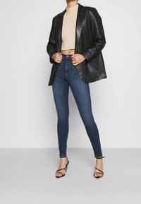 Svart läderblazer, beige ribbad kort tröja, blå skinny jeans och svarta sandaler med hög klack och remmar.