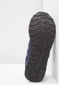 Marina sneakers med en texturerad svart gummisula med ett unikt mönster, syntetiskt övermaterial och dekorativa detaljer på sidorna.