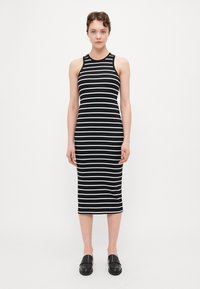 Sorte og hvite stripete ermeløs kjole med en tettsittende silhuett, ribbestruktur, som når midt på leggen, kombinert med svarte slip-on sko.