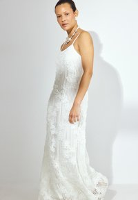 Witte, mouwloze jurk met bloemenkantdetails, een losse pasvorm en een rechte silhouet. Versterkt met een chunky parelketting.
