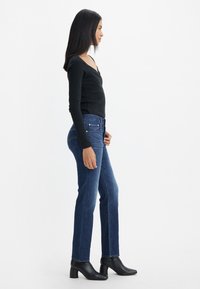 Maglietta nera a maniche lunghe, con design aderente. Jeans blu a gamba dritta con stile classico a cinque tasche. Stivali neri alla caviglia con punta squadrata.