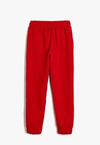 Rote Sweatpants aus weichem Material, mit einem elastischen Bund und elastischen Bündchen an den Knöcheln, in entspannter Passform und ohne sichtbare Muster.