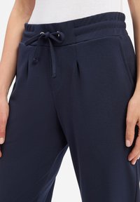 Granatowe dresy z elastycznym pasem, sznurkiem do regulacji i bocznymi kieszeniami, charakteryzujące się gładką, miękką fakturą.