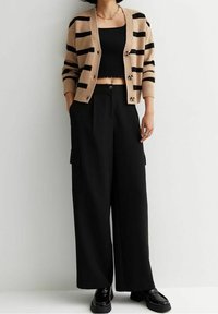 Cardigan rayé marron clair et noir, haut court noir et pantalon large noir avec poches à soufflet. Chaussures en noir brillant.