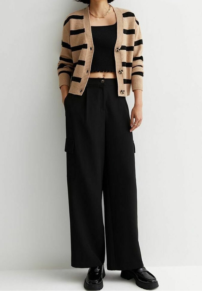 Cardigan rayé marron clair et noir, haut court noir et pantalon large noir avec poches à soufflet. Chaussures en noir brillant.