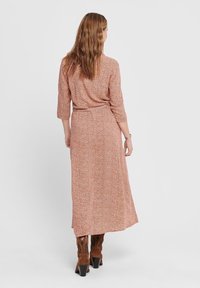 Maximekkok, jossa on istuva vyötärö, kolmen neljänneksen hihat ja pieni kukkakuosi ruosteisissa ja kermansävyissä. Sujuva kangas, jossa on ilmava siluetti.