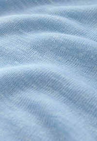 Miękki, jasnoniebieski dzianinowy materiał o drobnych, równych ściegach i delikatnych fałdach tworzących subtelną teksturę i cienie.