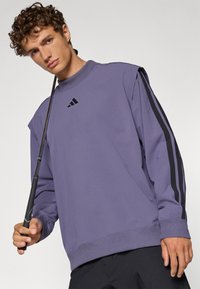 Felpa viola con strisce nere laterali e logo Adidas sul petto. Presenta un collo alto e polsini a coste, design semplice.