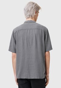 Grijze shirt met korte mouwen van een gestructureerde stof. Heeft een puntig kraag en een rechte zoomlijn, met een relaxte pasvorm en zijsplitsingen.