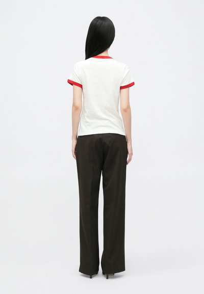 Biała koszulka z czerwonym ściągaczem przy kołnierzyku i rękawach, w zestawieniu z luźnymi czarnymi spodniami, widziana z tyłu.
