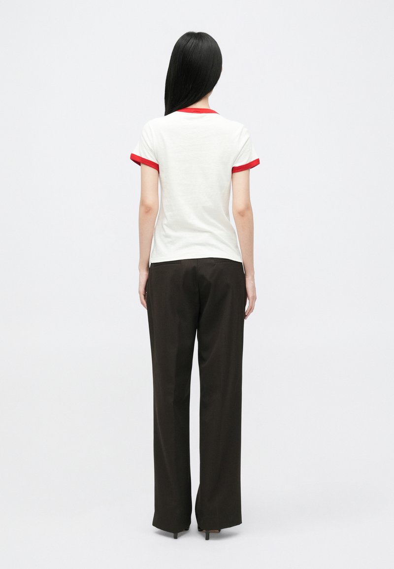 T-shirt blanche avec col et accents de manches rouges, associée à un pantalon noir ample, vue de dos.
