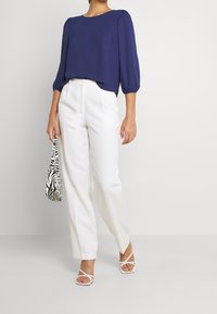 Blouse bleu marine, ample avec des manches trois-quarts, associée à un pantalon blanc ajusté. Accessoirisée avec un sac à motif zèbre.