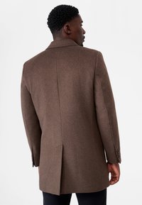 Brun ullblandad kappa med skräddarsydd passform, strukturerade axlar och en slits bak, med knäppda manschetter.