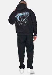 Black hoodie with a graphic scorpion design on the back, featuring the text “mist nobody." Paired with black pants and white sneakers.