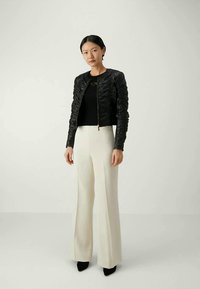 Una chaqueta bomber negra con textura y collar acanalado, combinada con pantalones de tiro alto y pernera ancha crema y tacones negros puntiagudos.