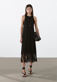 Černé žebrované šaty s třásňovým lemem, kulatým výstřihem a bezrukávovým designem. Doplněné texturovanou černou kabelkou a plochými sandály.
