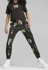 Svart kort t-shirt med grafisk tryck, parat med svarta joggers med färgglada mönster och logotyper, bärs med vita plattformsskor.