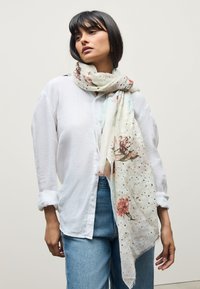 Kerge lillemustriga sall pehmes kreemjas toonis roosade ja roheliste aktsentidega, millel on narmendav serv ja õrn täpiline tekstuur.